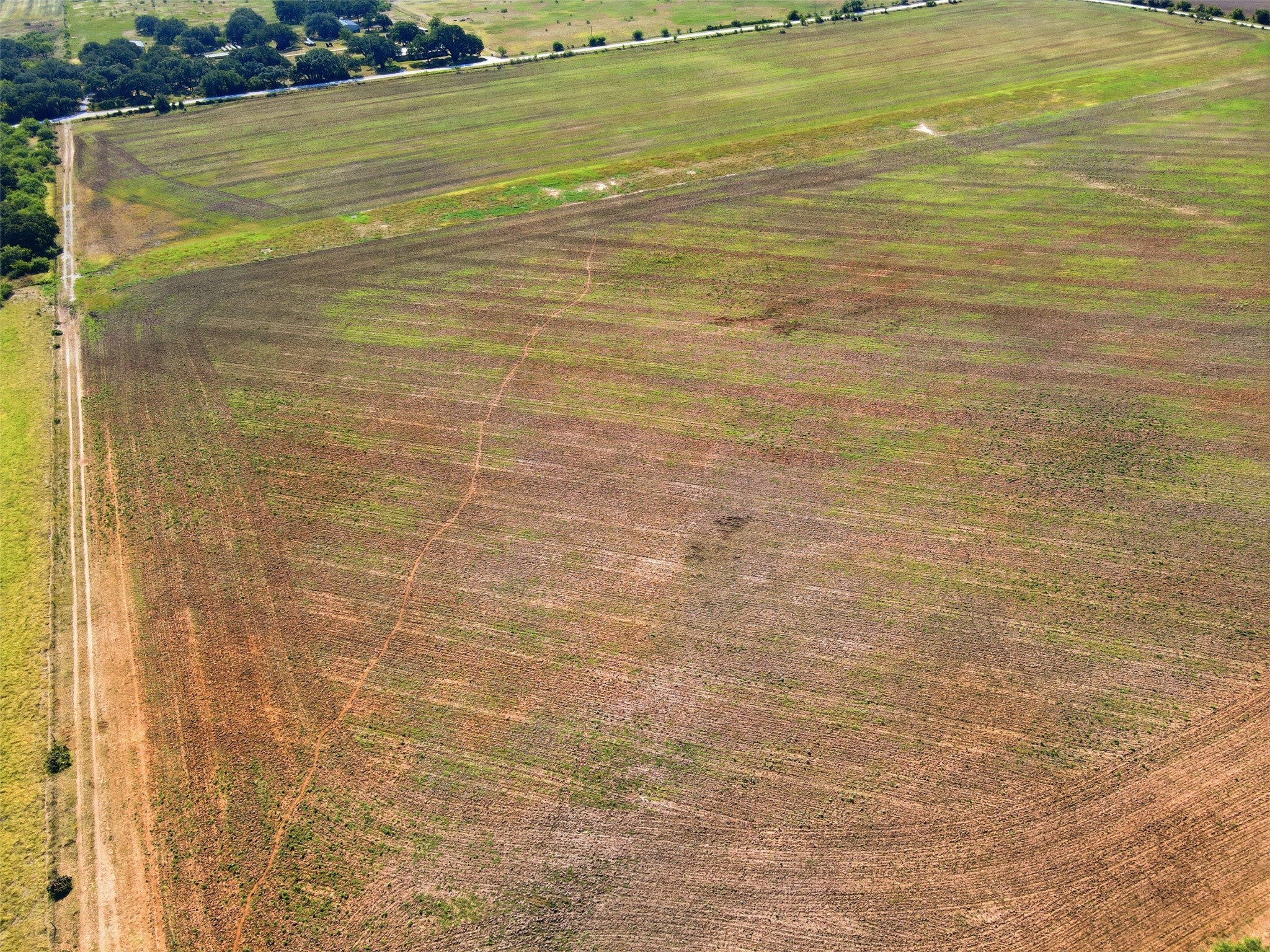 Aerial view of open rural fields with a dirt access road and distant tree line.