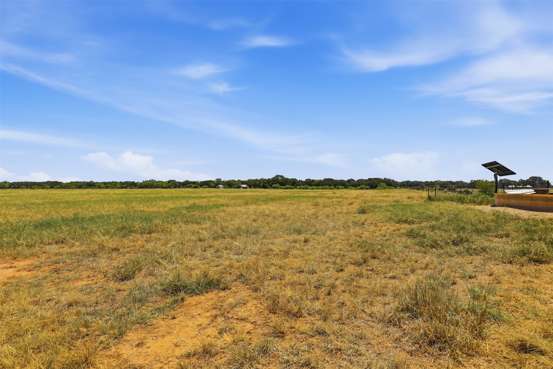 Open grassy acreage with a tree-lined horizon and a solar-powered water well beside a fence.