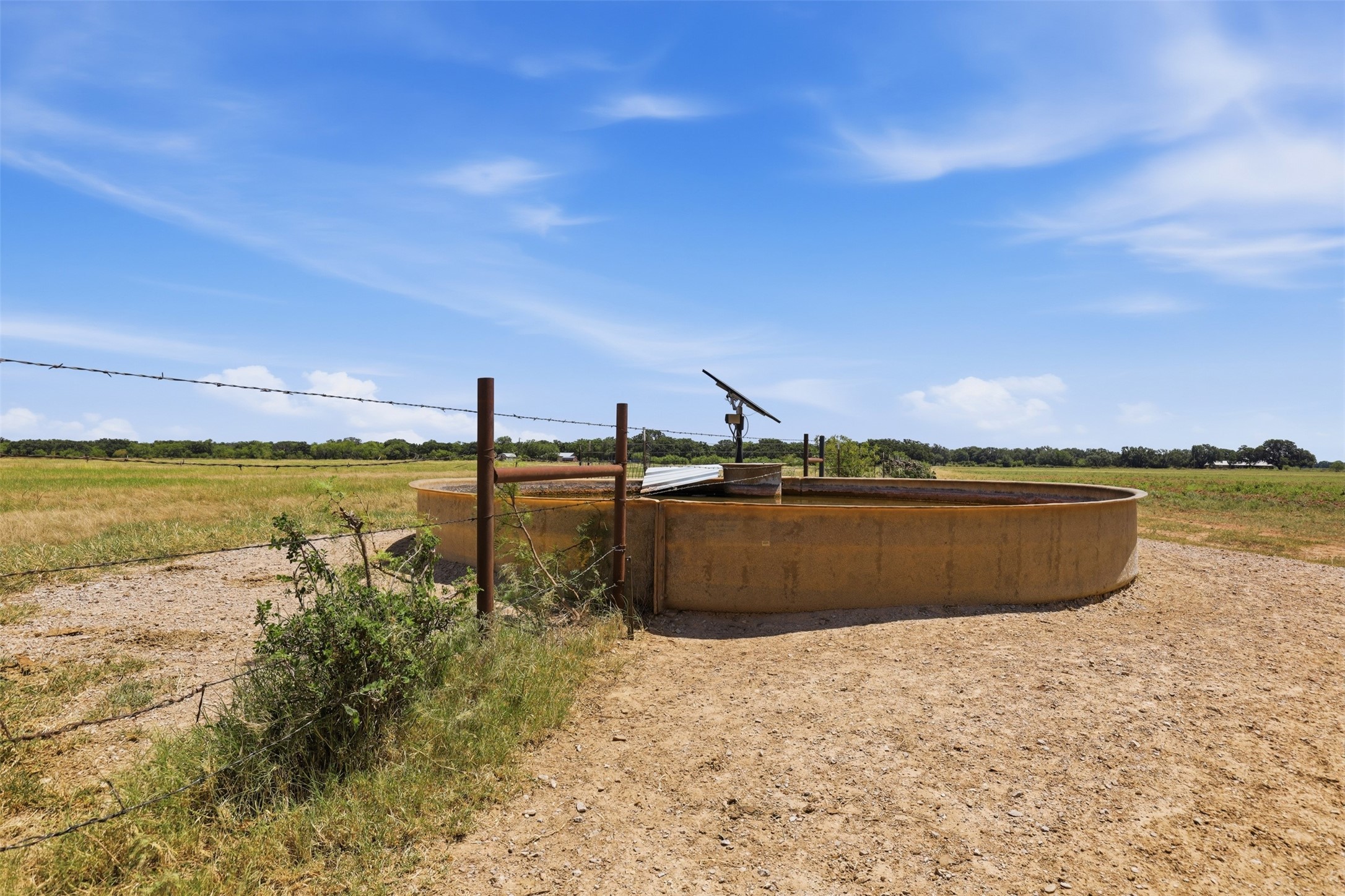 Livestock water trough and solar pump beside a fence in an open field.