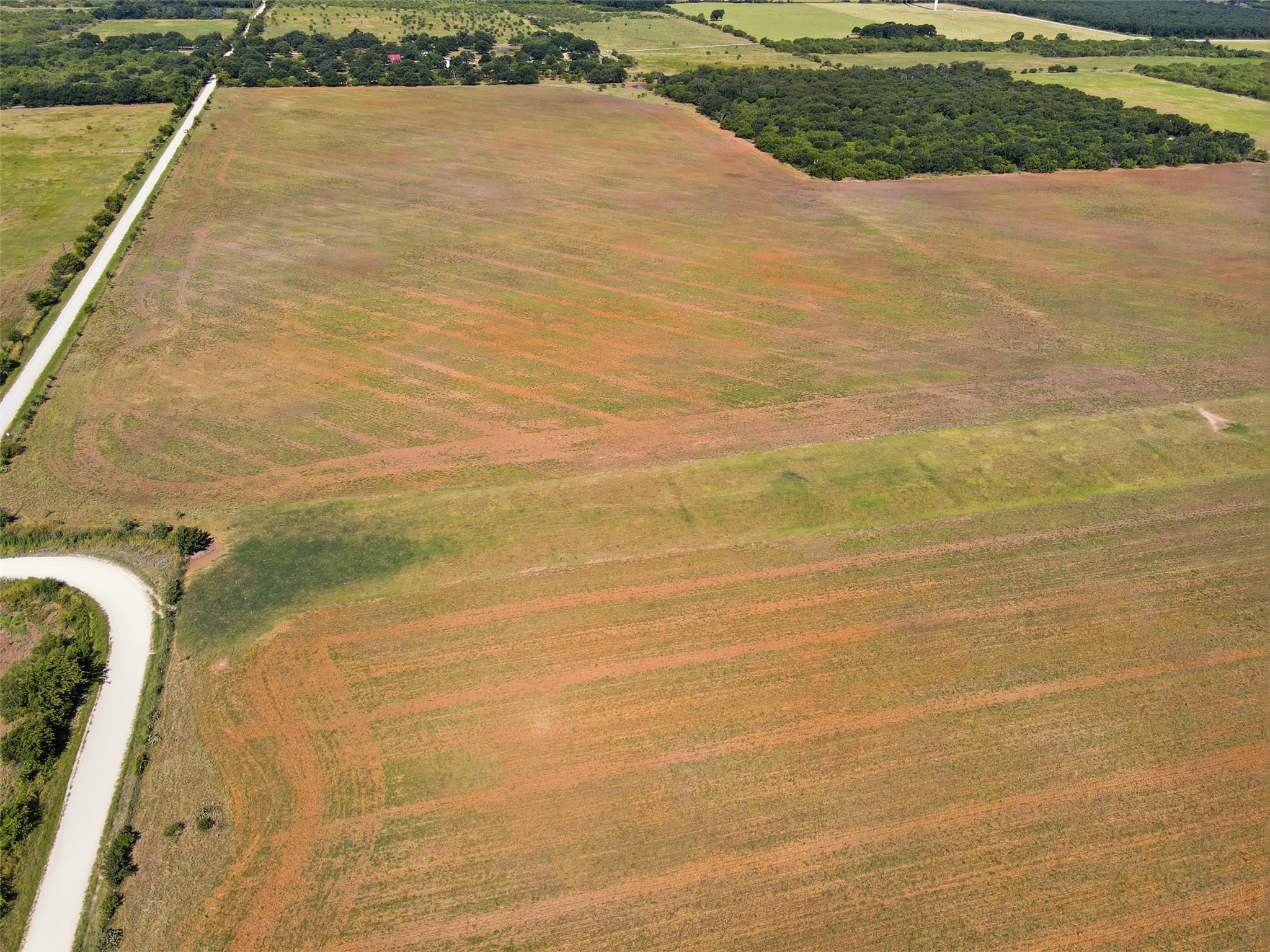 Aerial view of open acreage with fields, tree lines, and a curving rural road.