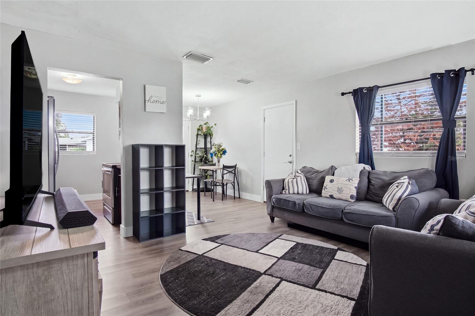 Living room with a gray sectional, geometric rug, and blue curtains beside a bright window.