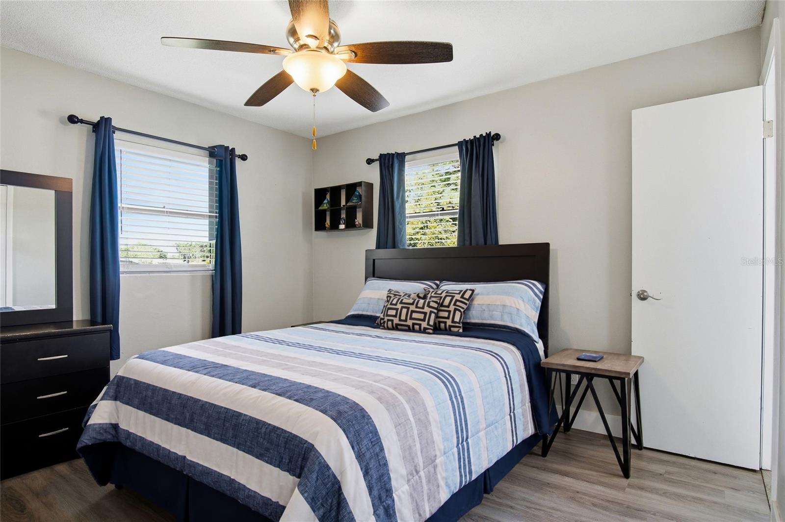 Bedroom with blue-and-white striped bedding, navy curtains, and a dark wood bed.