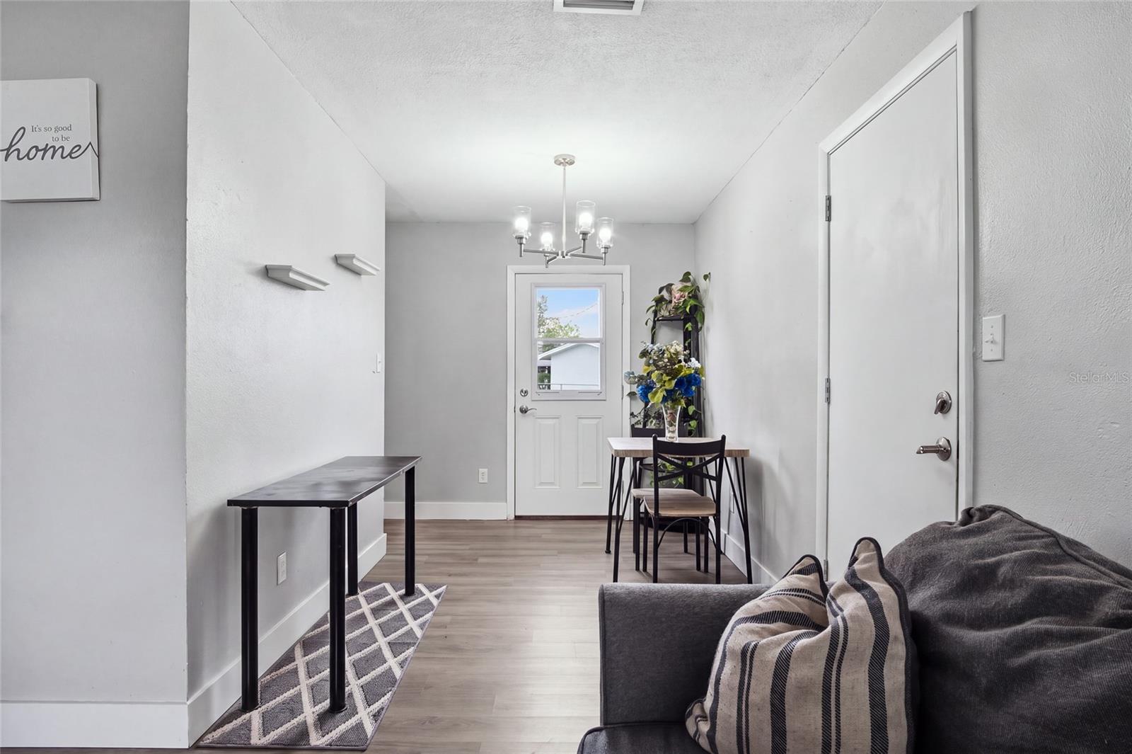 Furnished entry and dining area with a white door, small table, chandelier, and gray sofa.