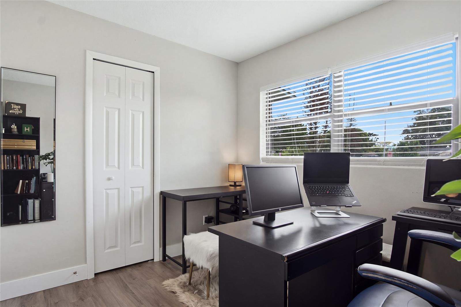 Furnished home office with two computer workstations and wide windows overlooking trees.