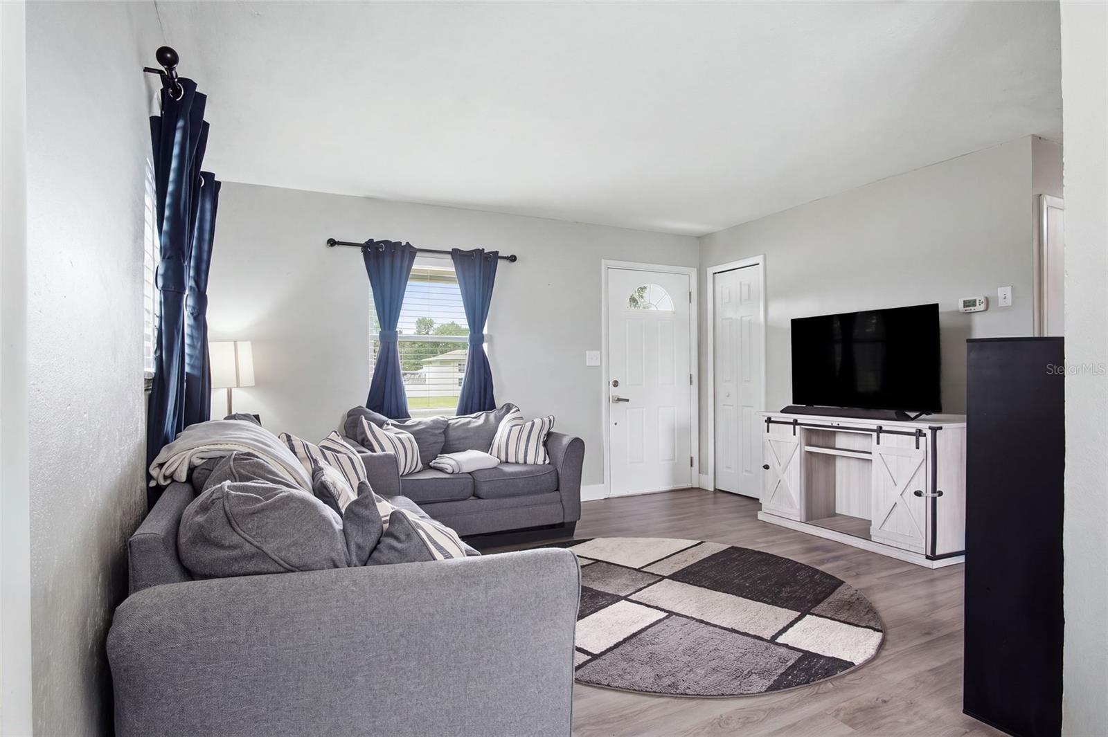 Living room with gray sofas, navy curtains, geometric rug, and television on a white console.