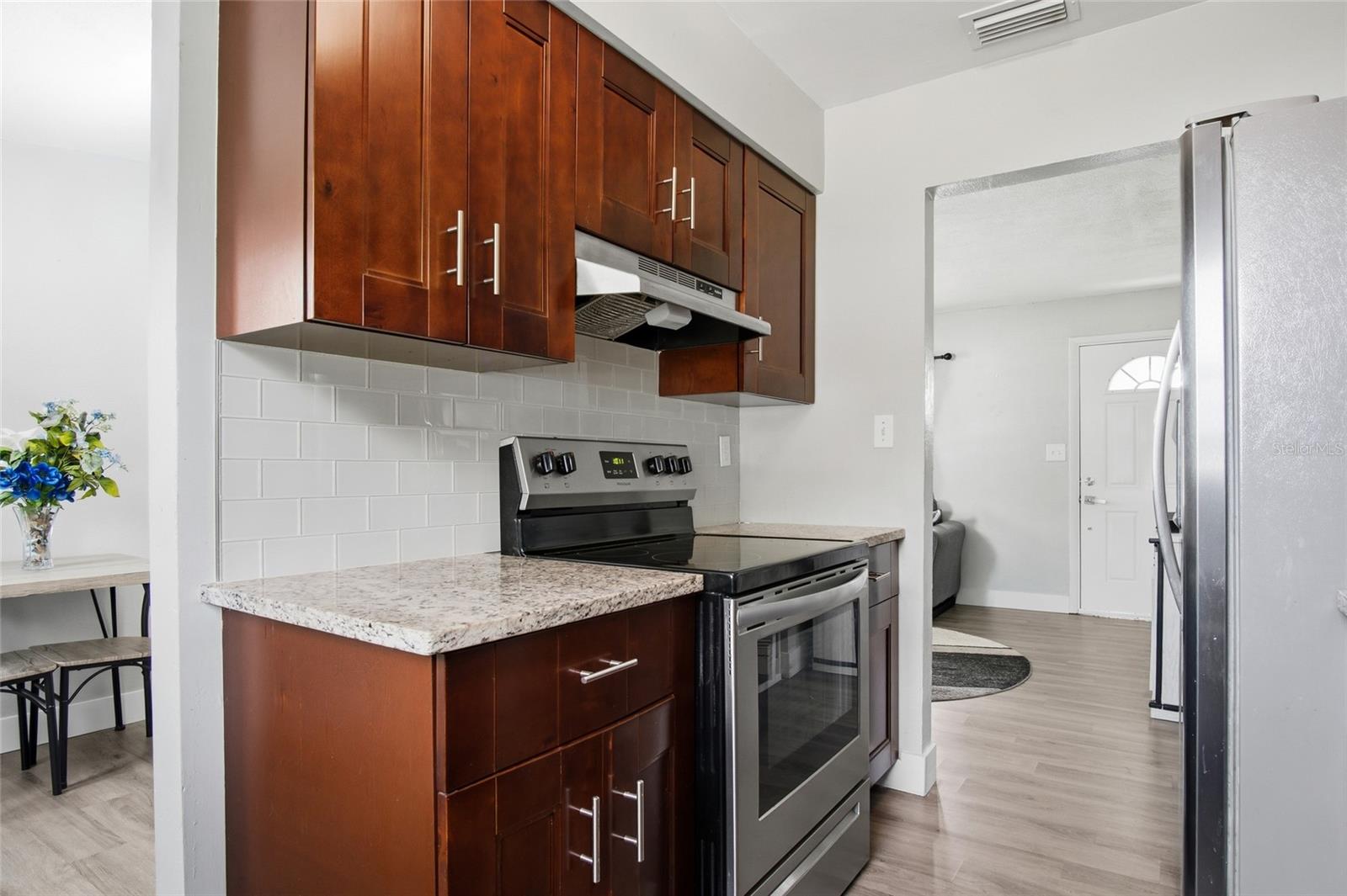 Kitchen with dark wood cabinets, granite counters, white tile backsplash, and stainless-steel appliances.