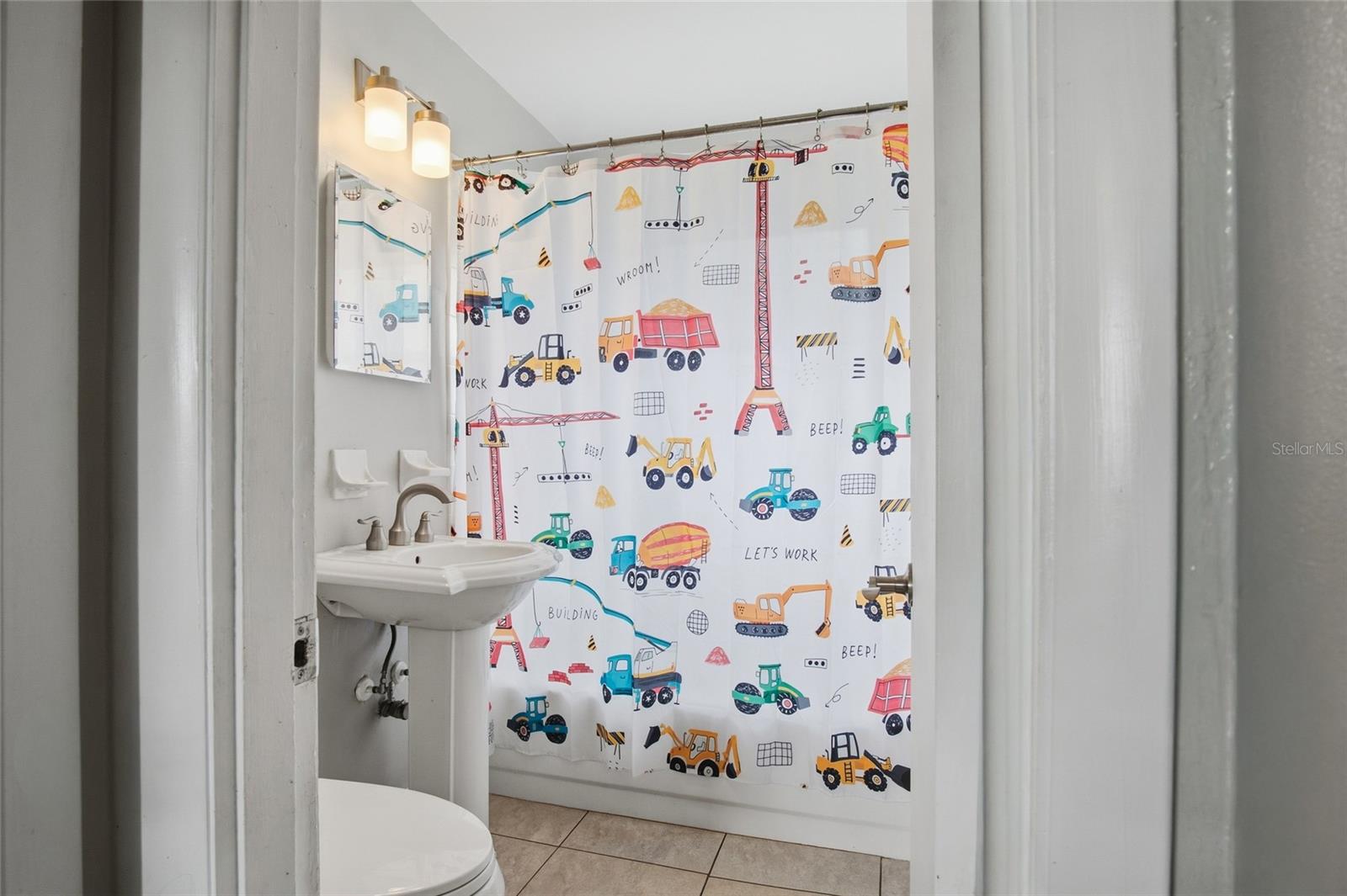 Bathroom with a pedestal sink and a colorful construction vehicle shower curtain.