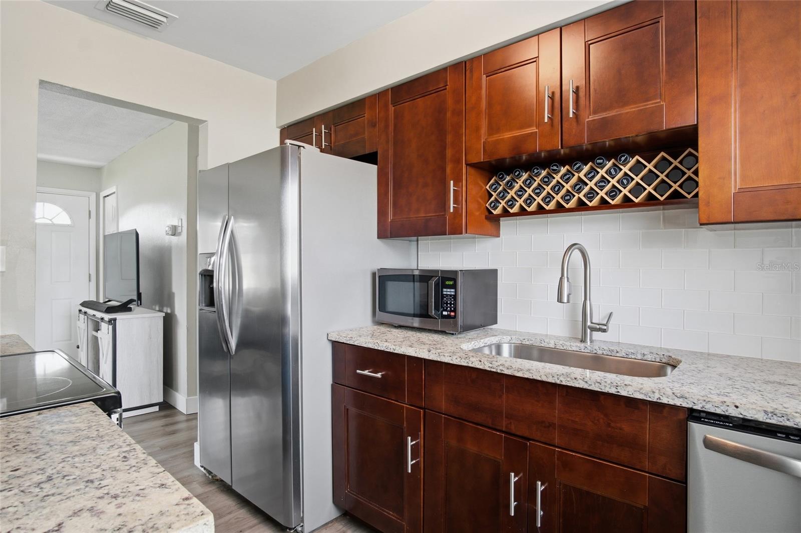 Kitchen with dark wood cabinets, built-in wine rack, white tile backsplash, and stainless steel appliances.