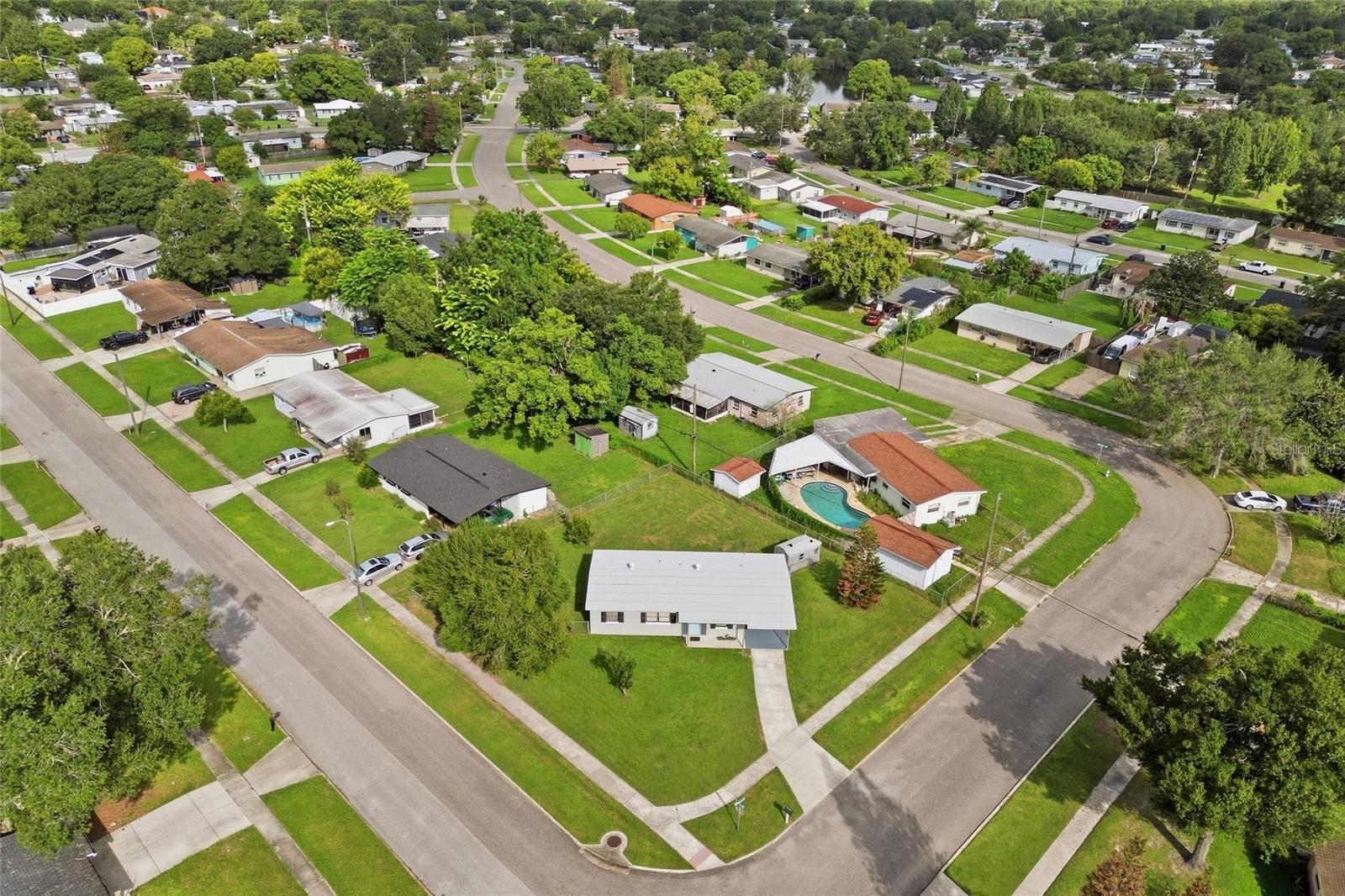Aerial view of a light-roofed home on a grassy corner lot in a tree-lined neighborhood.