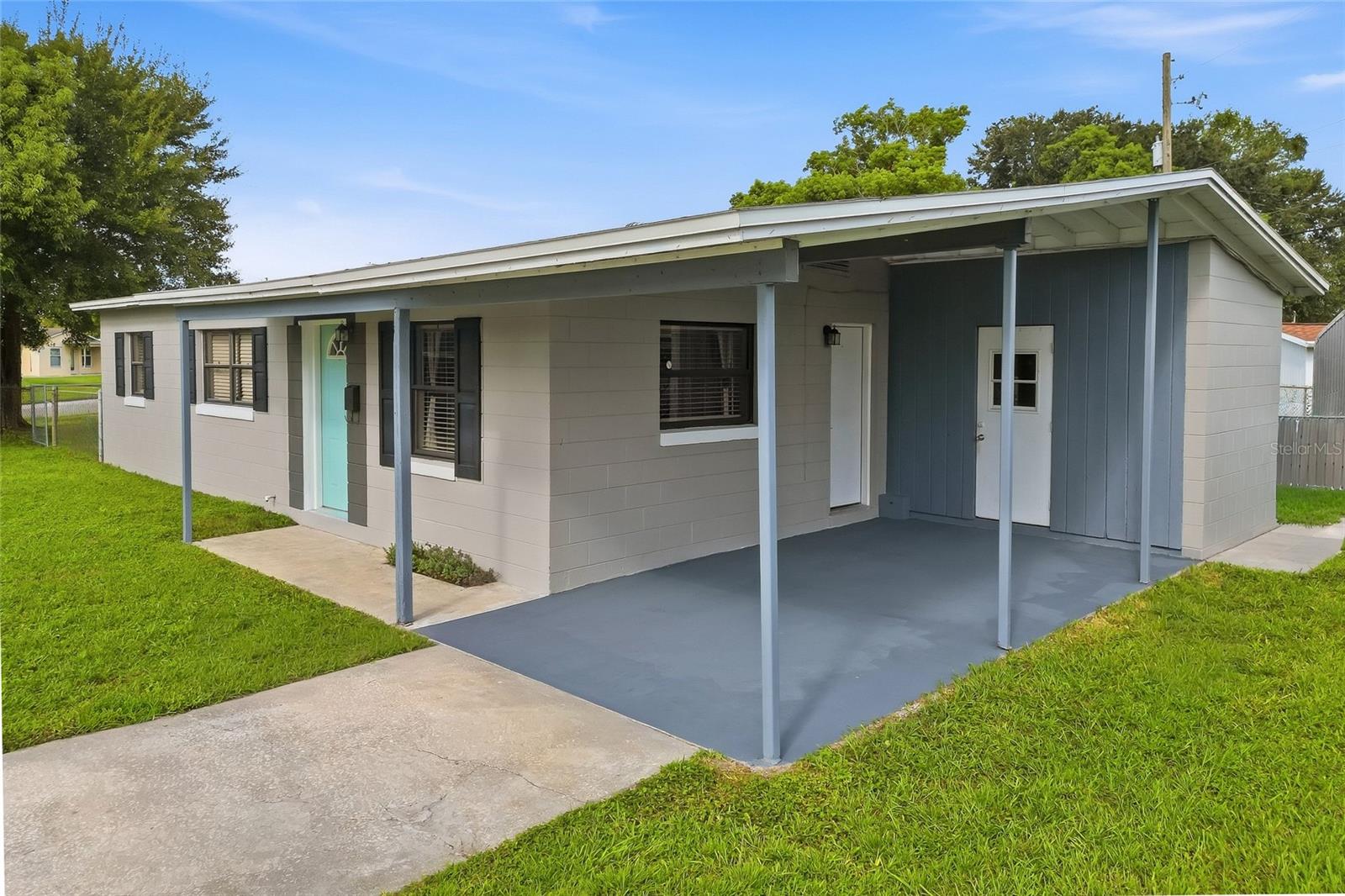 Single-story home with a broad covered carport, blue accent wall, and turquoise front door.