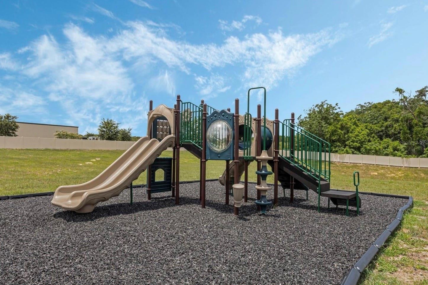 Community playground with tan slides and climbing platforms on a rubber mulch surface.