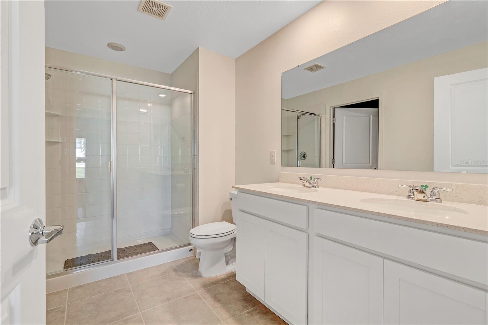 Bathroom with a glass-enclosed shower and a long white double-sink vanity.