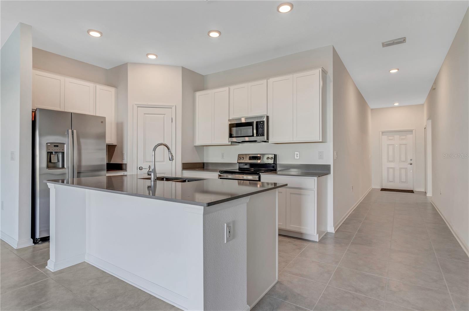 Kitchen with a large island, white cabinetry, stainless steel appliances, and gray tile floors.