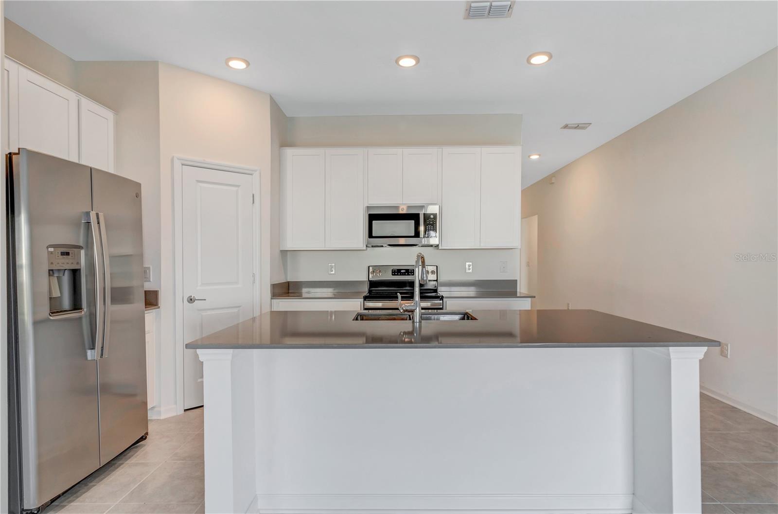 Kitchen with white cabinetry, stainless steel appliances, and a large gray-topped island with sink.