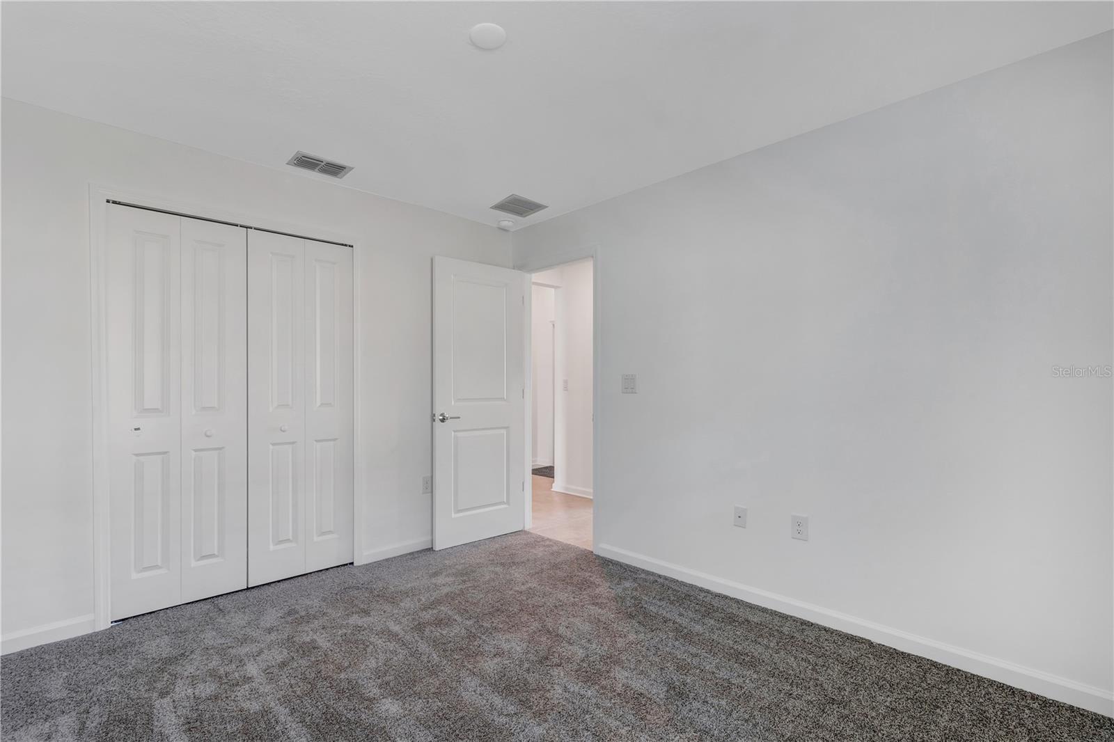 Empty bedroom with gray carpet, white walls, and a double-door closet.