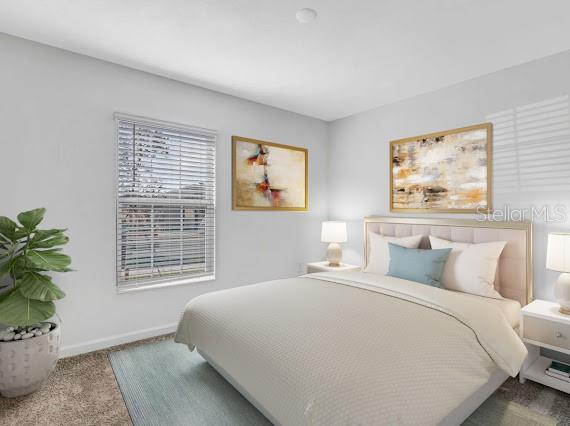 Bedroom with a pale upholstered headboard, blue accent pillow, abstract art, and a potted plant.