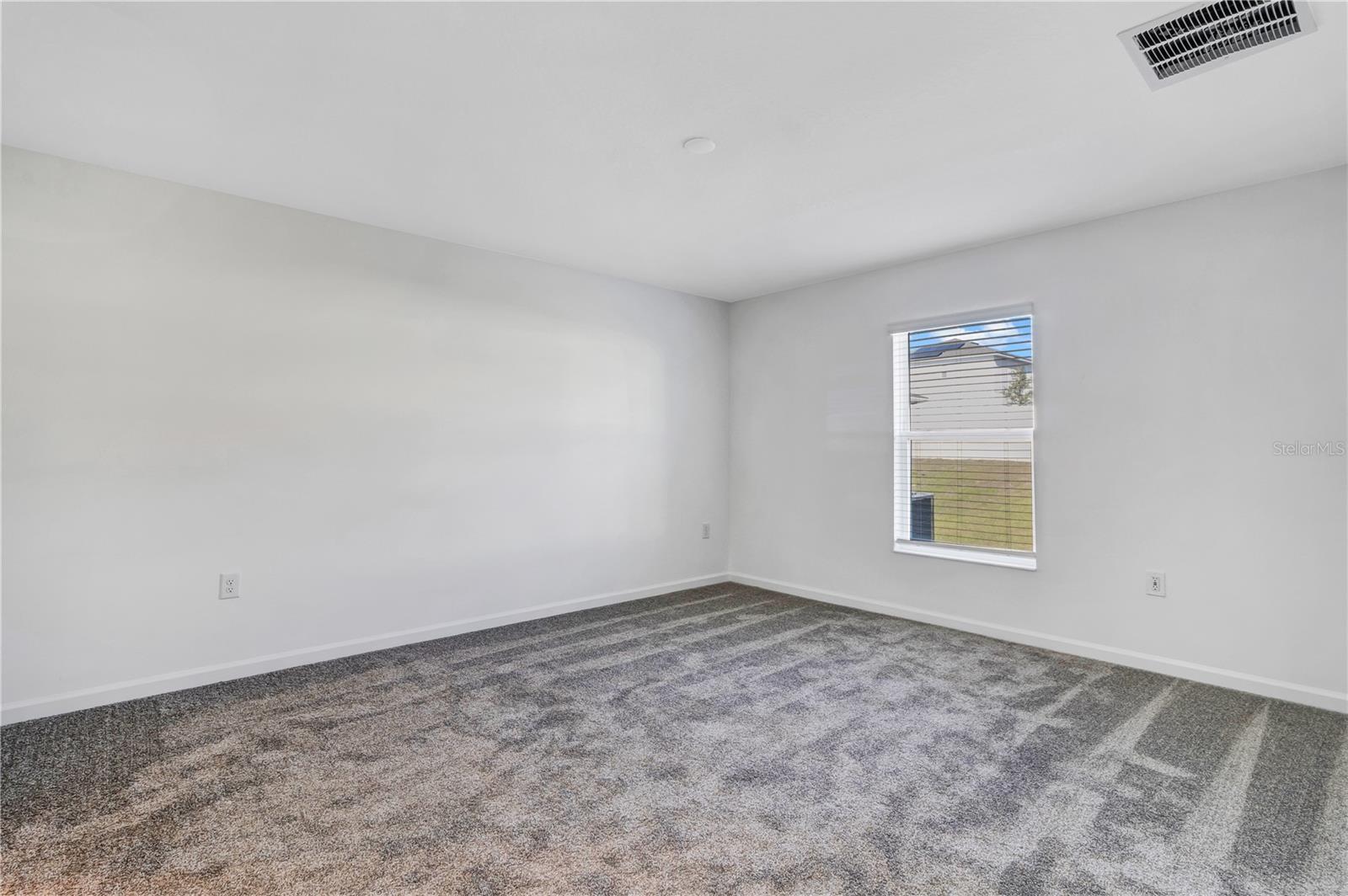 Empty bedroom with patterned gray carpet and a window overlooking the lawn.