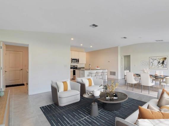 Open-plan living room with white chairs, a dark striped rug, and kitchen island.