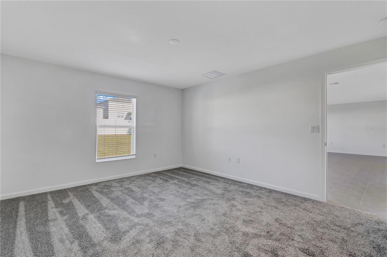 Empty carpeted room with a window and an open doorway to a tiled area.