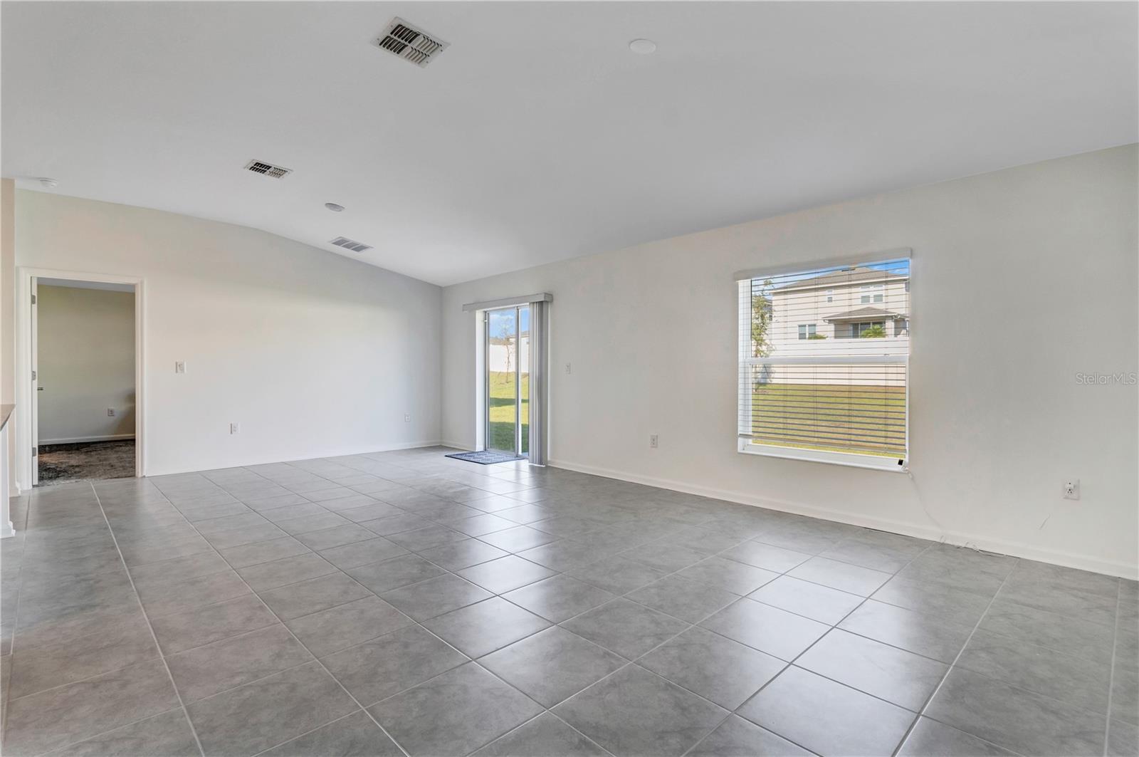 Vacant living room with gray tile floors, a wide window, and a sliding glass door to the yard.