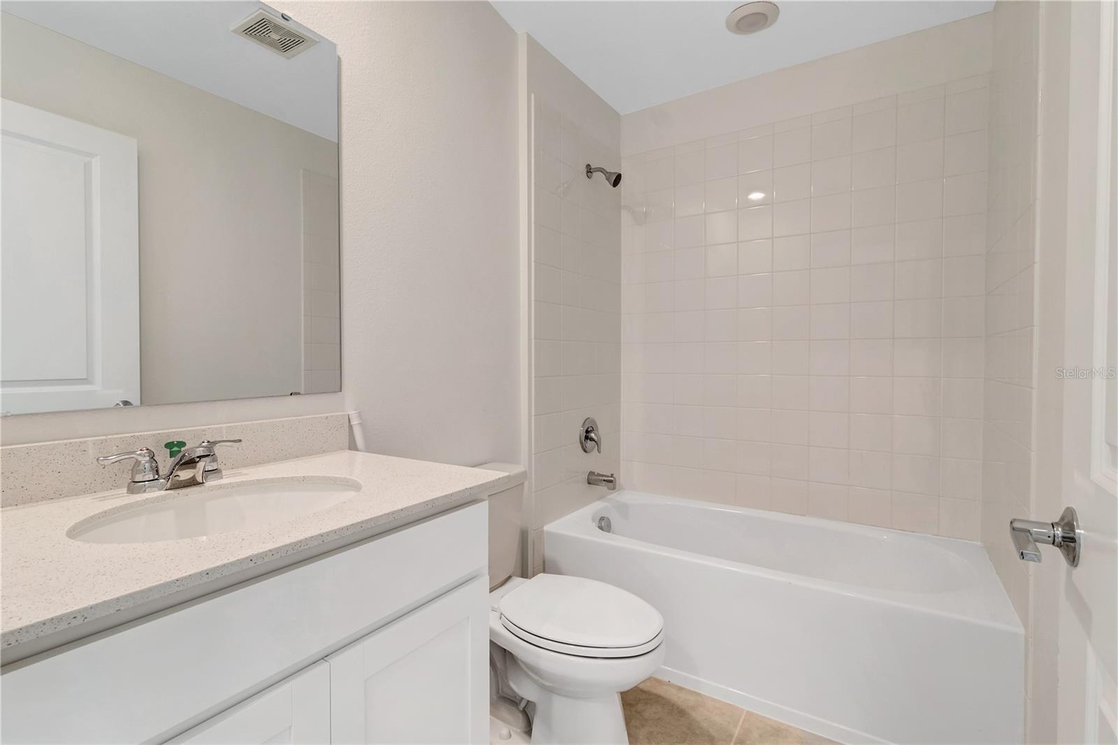 Bathroom with a white vanity, toilet, and bathtub beneath a tiled shower surround.