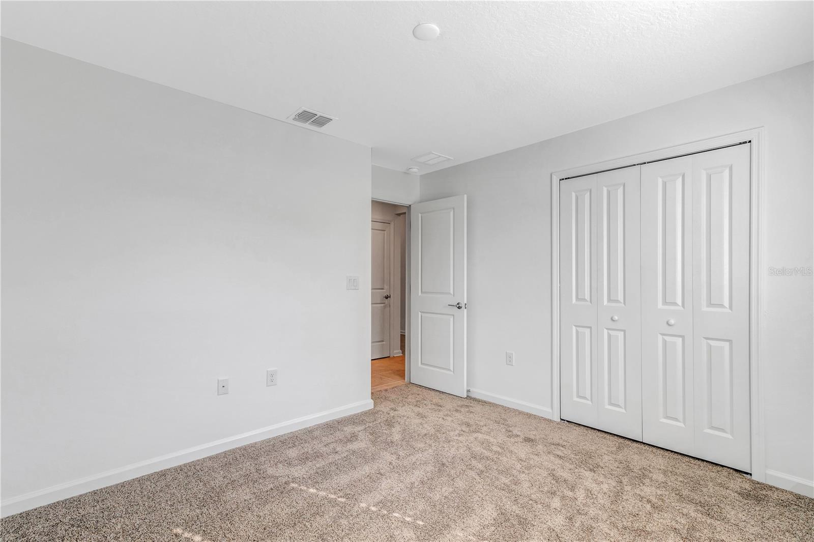Empty bedroom with beige carpet, white walls, and a double-door closet.