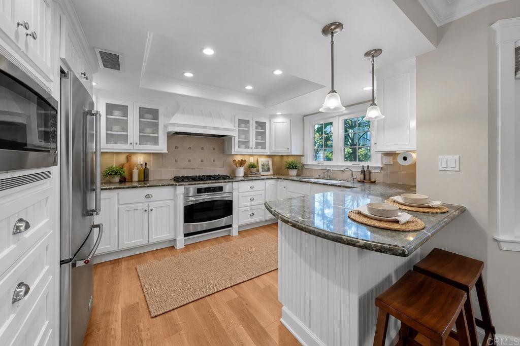 Bright white kitchen with stainless steel appliances, stone island, and two wooden stools.