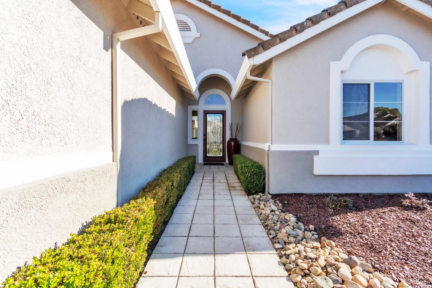 Home's covered front entry with a tiled walkway, trimmed hedges, and decorative glass door.