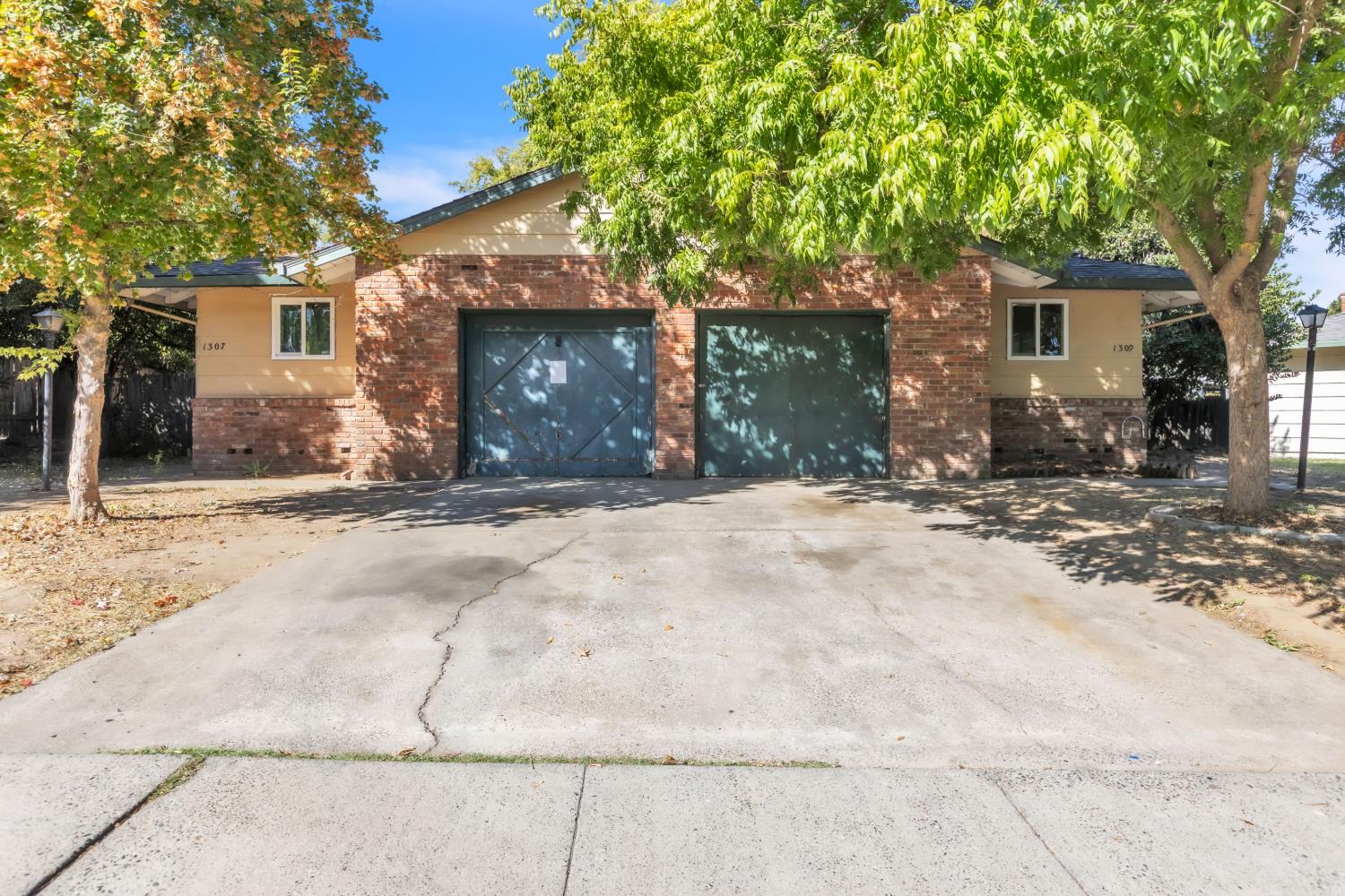Brick-and-tan building with two garage doors beneath mature shade trees.