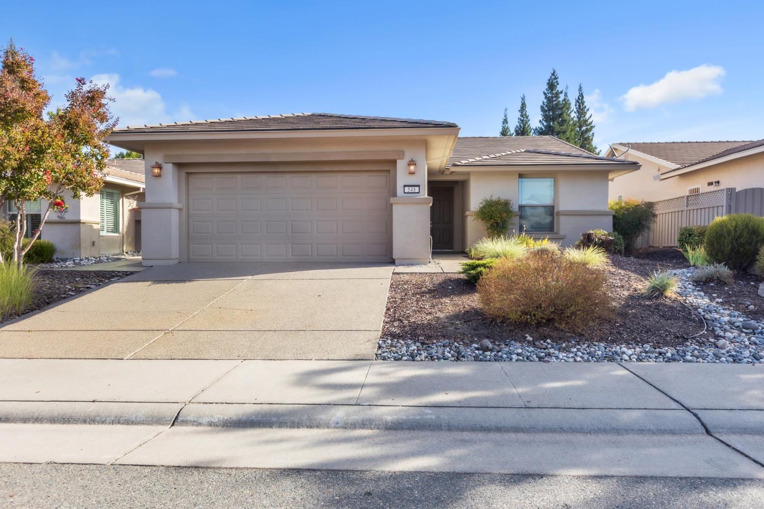 Single-story stucco home with a two-car garage, tiled roof, and landscaped rock garden.