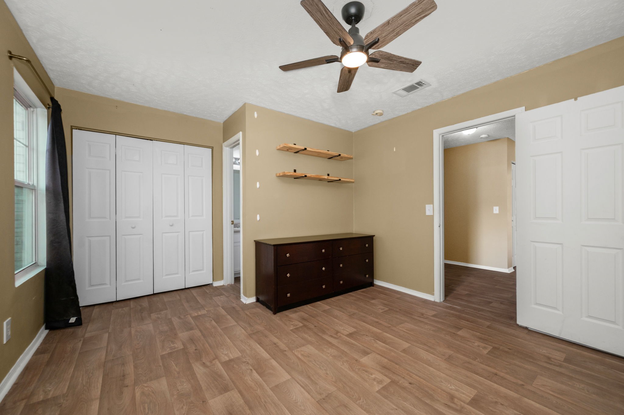 Bedroom with white closet doors, a dark dresser, floating shelves, and wood-look flooring.