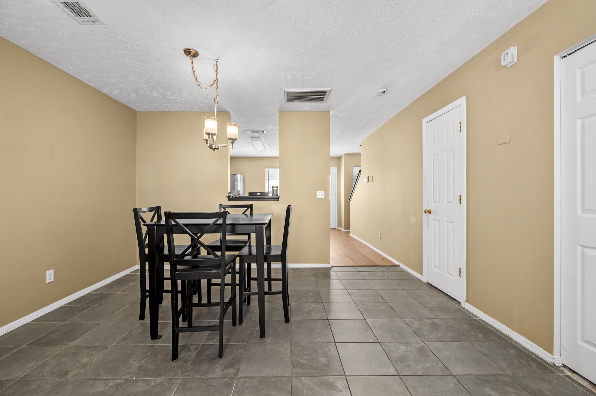 Dining area with a black table and chairs, gray tile floor, and kitchen pass-through.