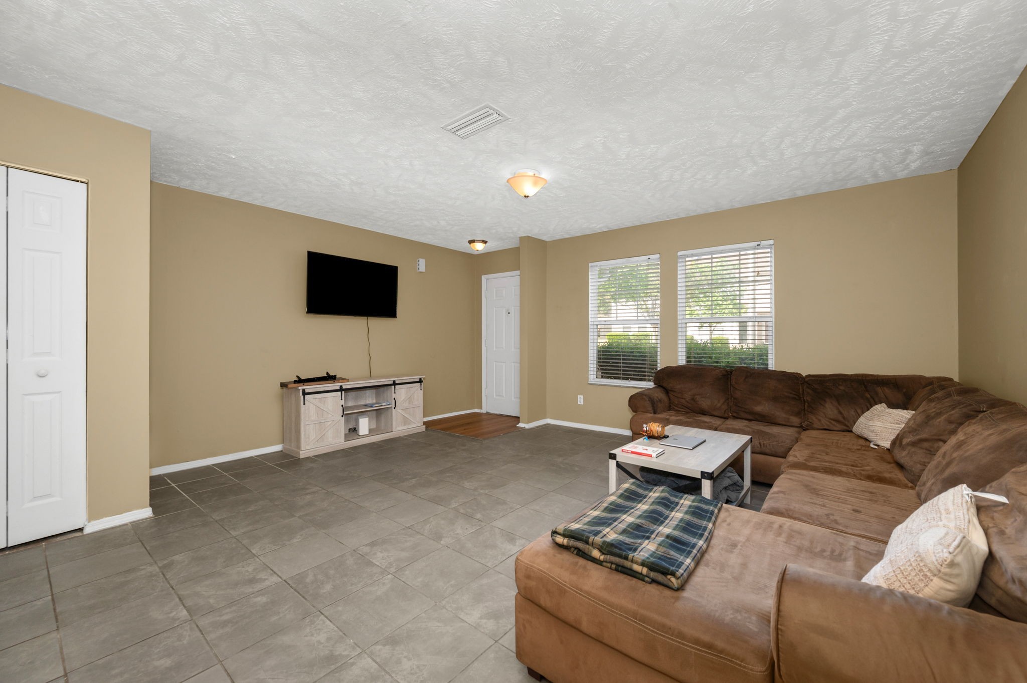 Living room with a brown sectional sofa, gray tile floor, and wall-mounted television.