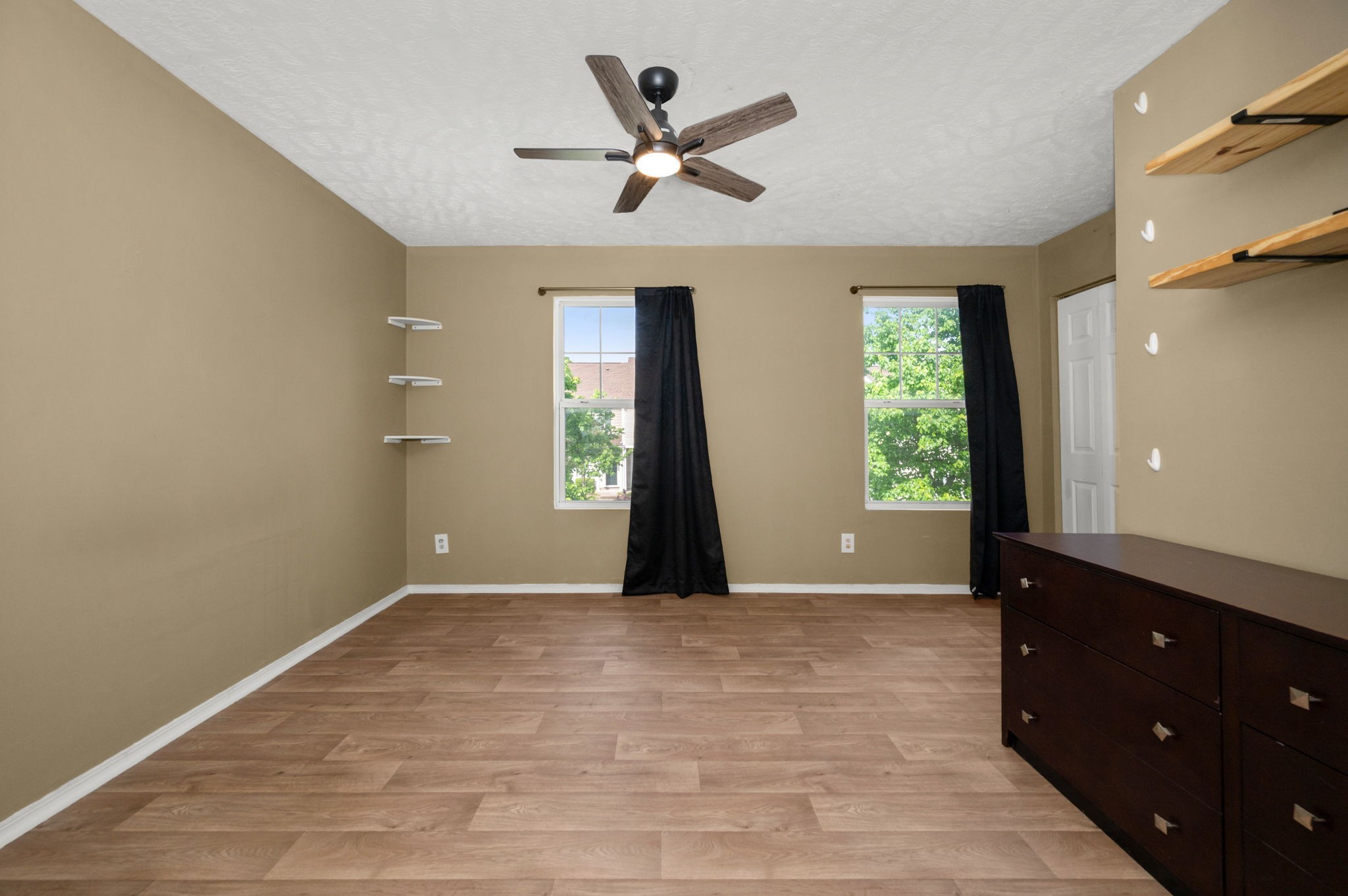 Bedroom with wood-look flooring, two curtained windows, and a dark dresser.