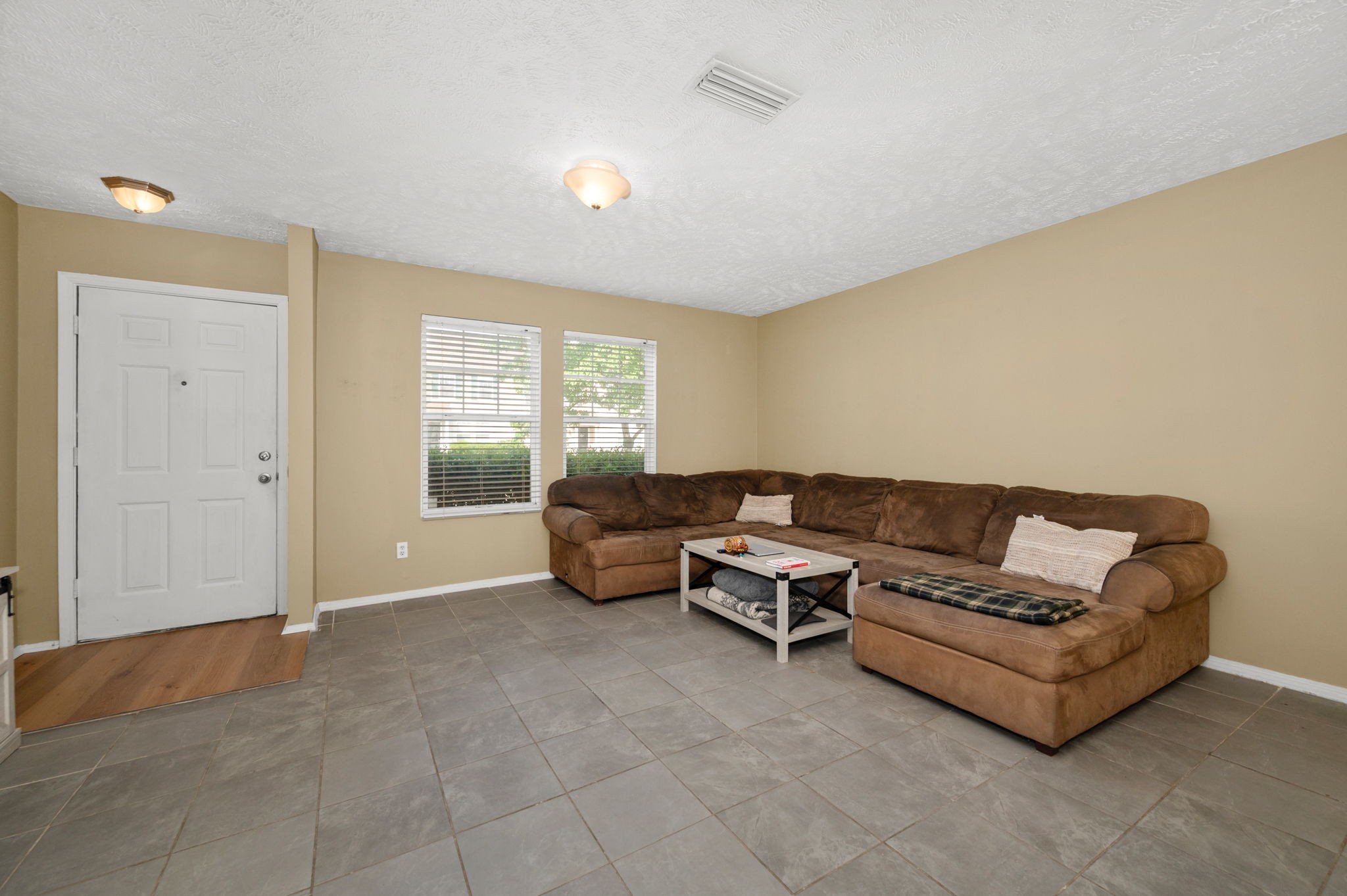 Living room with a large brown sectional, gray tile floors, and two windows beside the entry door.