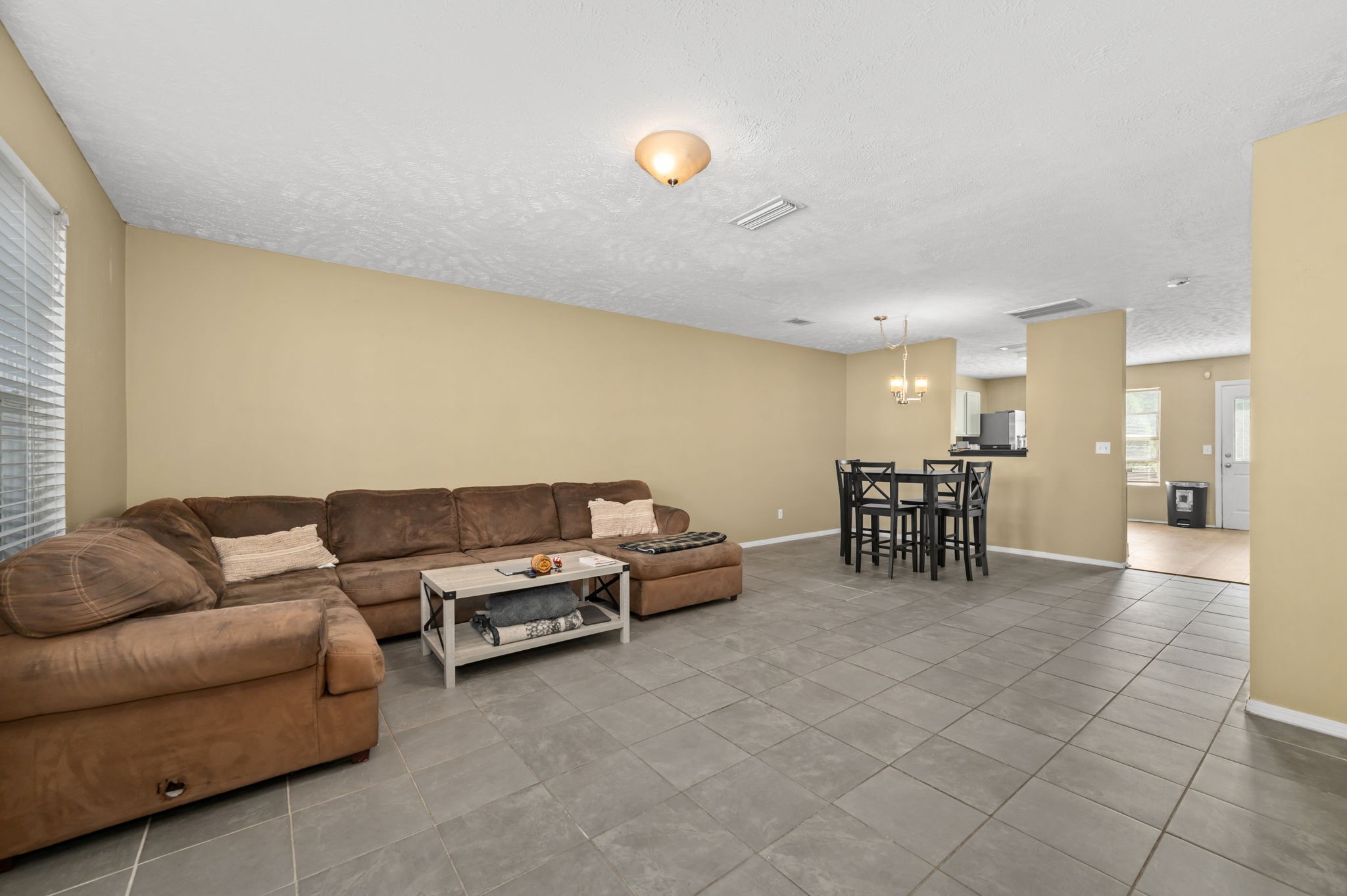 Living and dining area with a brown sectional, gray tile floors, and a high table with black chairs.