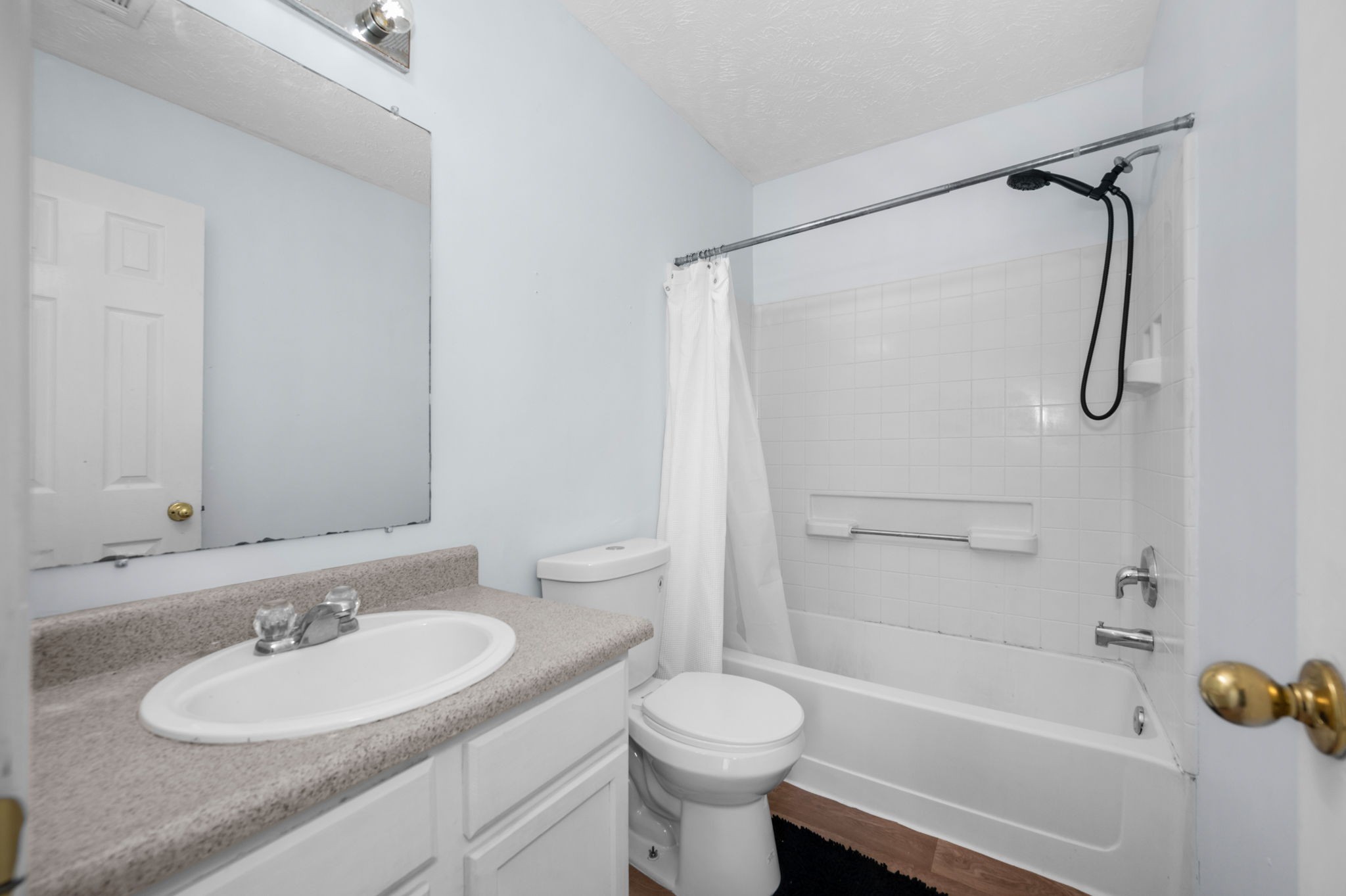 Bathroom with a granite-look vanity, toilet, and tiled tub-shower with grab bar.