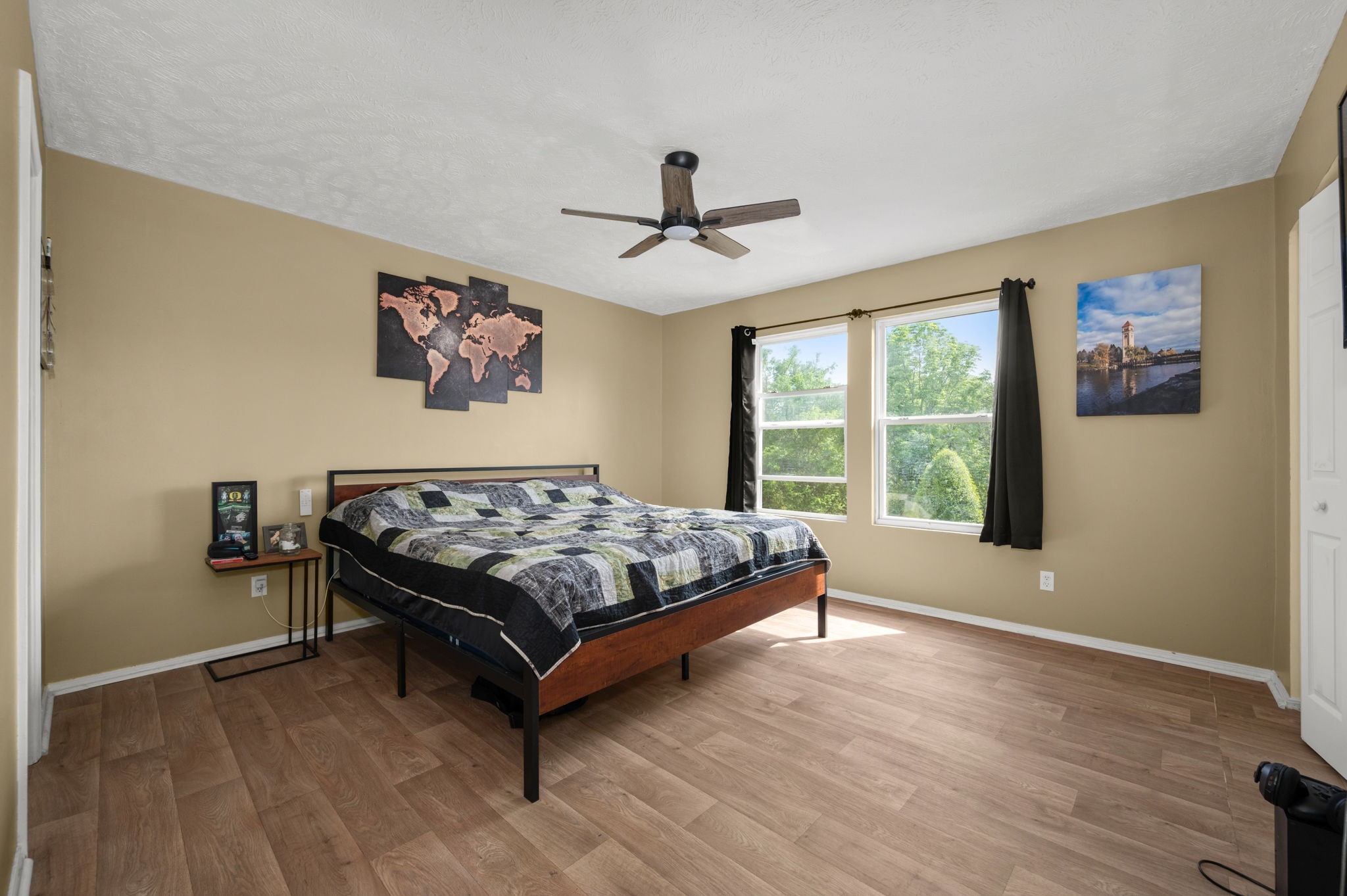 Bedroom with a large wooden bed, patchwork quilt, ceiling fan, and two curtained windows.