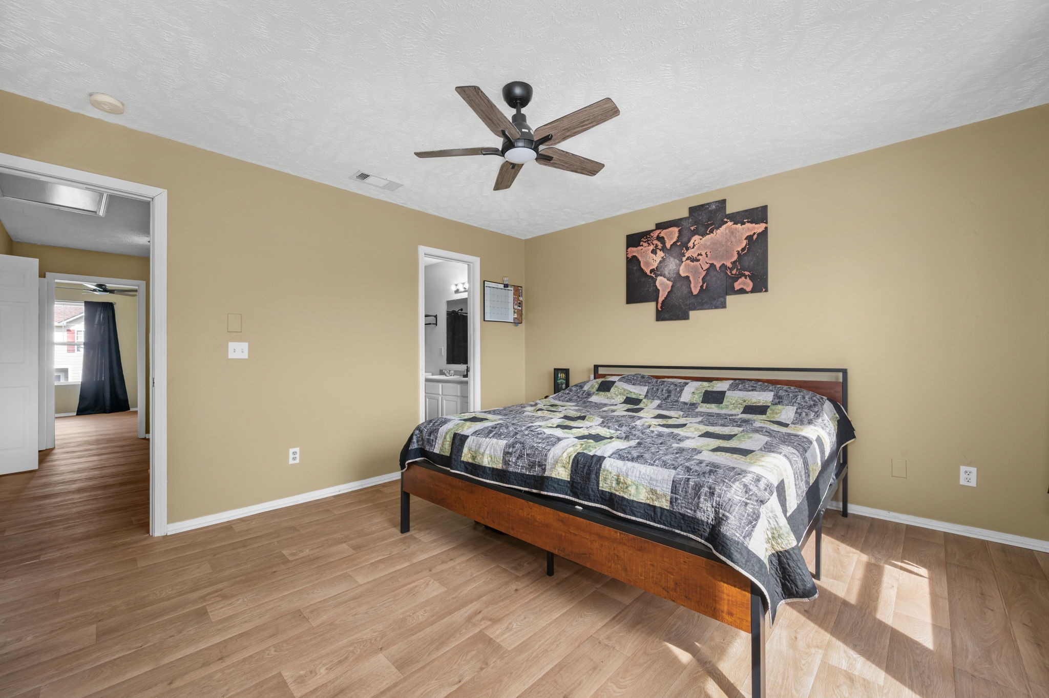 Bedroom with a wood-frame bed, gray patchwork quilt, ceiling fan, and world map wall art.