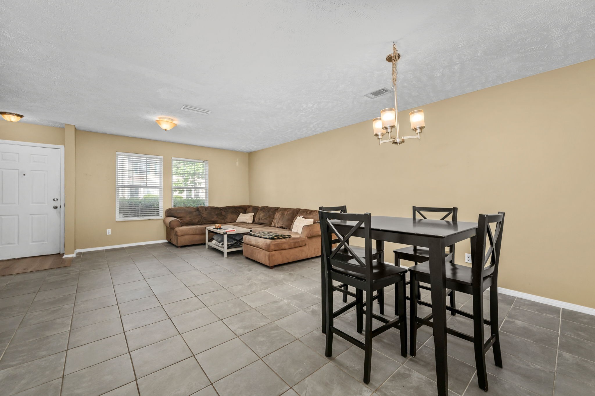 Living and dining area with a brown sectional, tiled floors, and a black dining table.