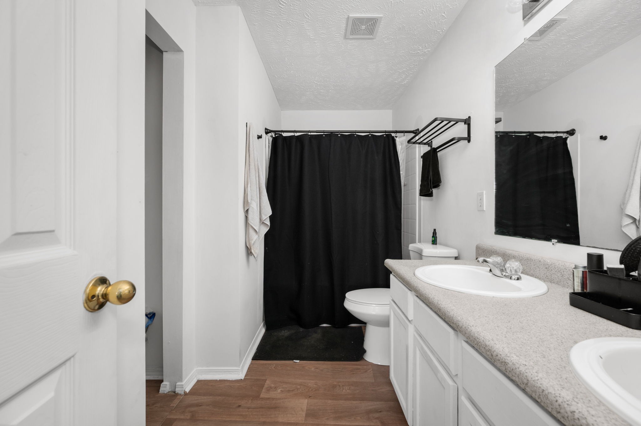 Bathroom with a long vanity, speckled countertop, and black shower curtain.