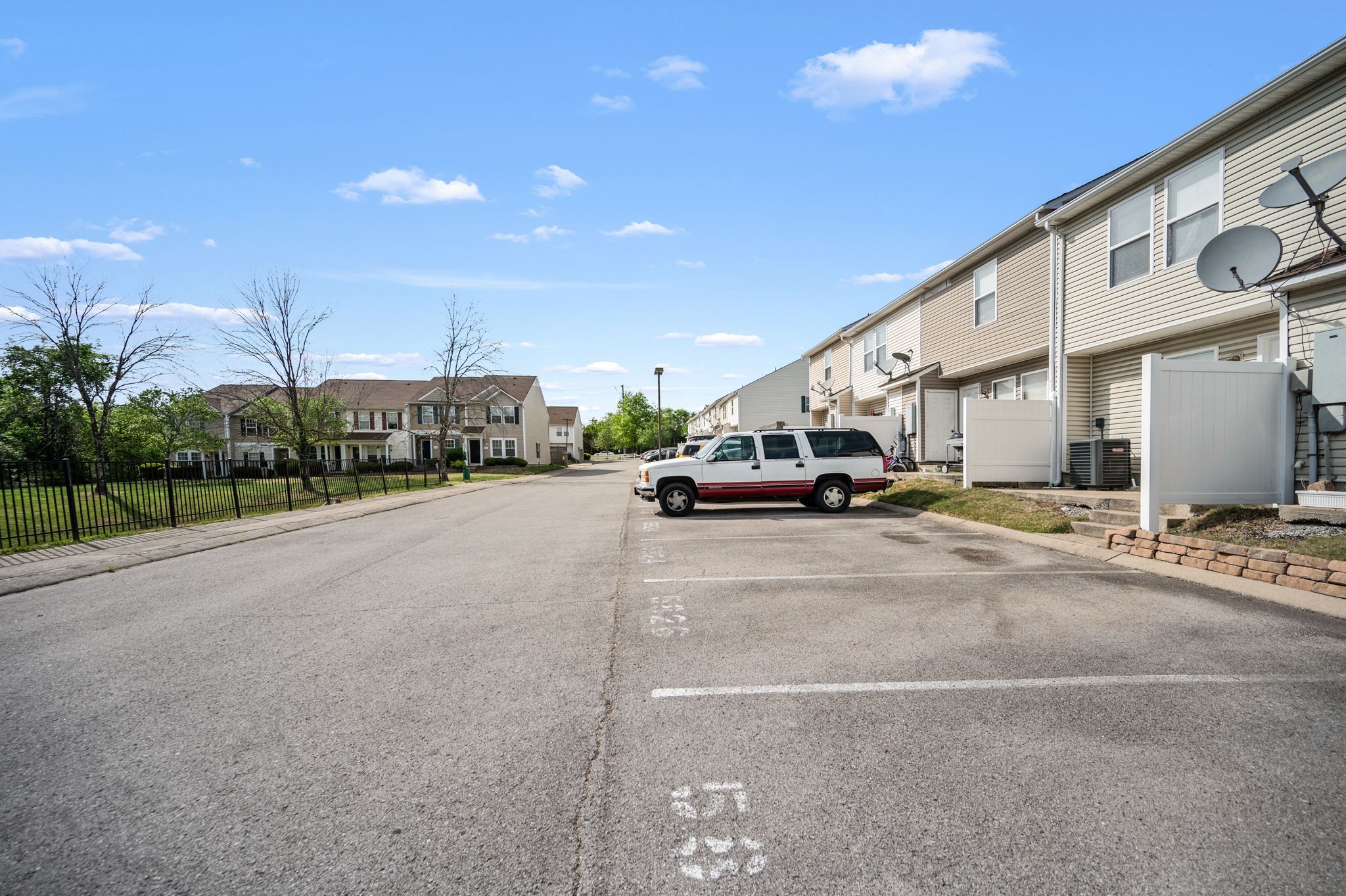Townhouse community beside a paved parking area, with fenced patios and a white SUV.