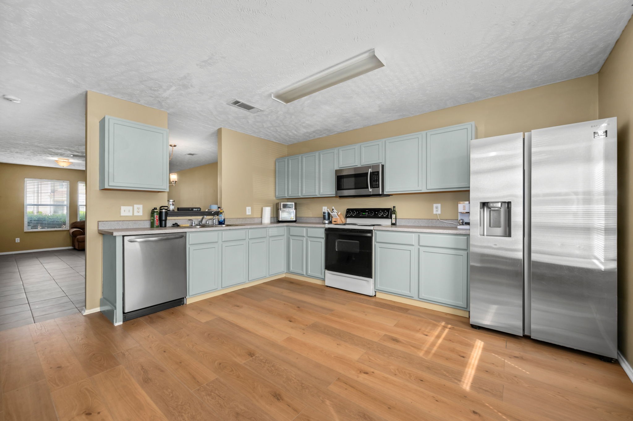 Kitchen with pale blue-gray cabinets, stainless steel appliances, and warm wood-look flooring.