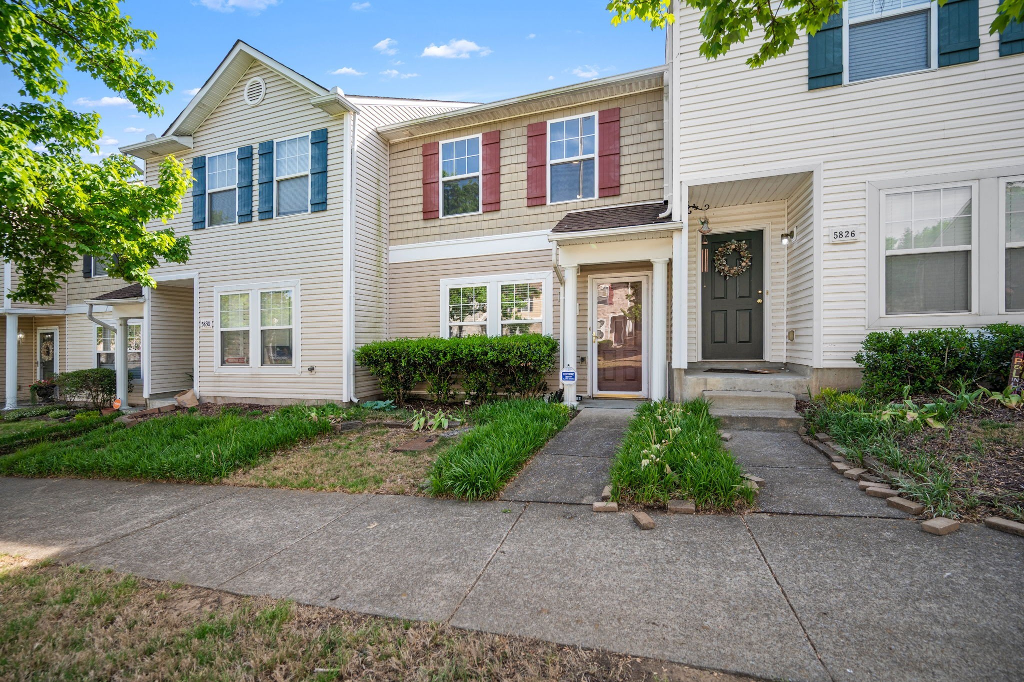 Beige two-story townhouse with contrasting shutters, a dark front door, and a landscaped front walkway.
