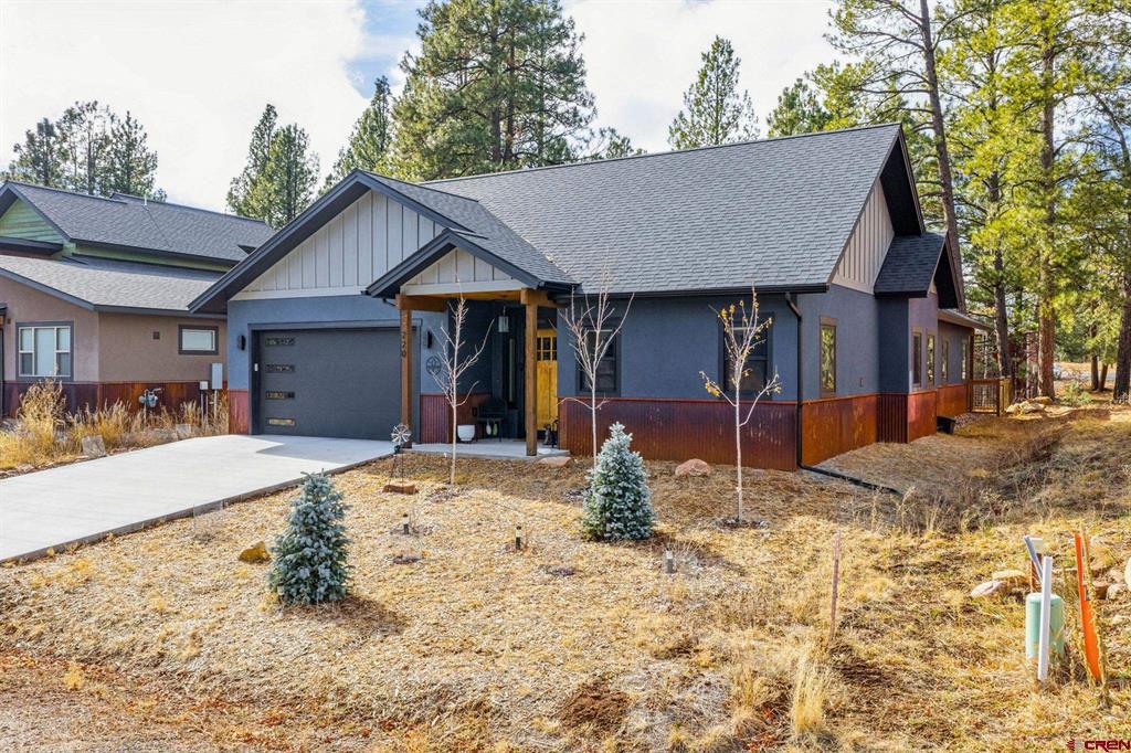 Blue-gray home with an attached garage and covered entry, surrounded by pine trees.