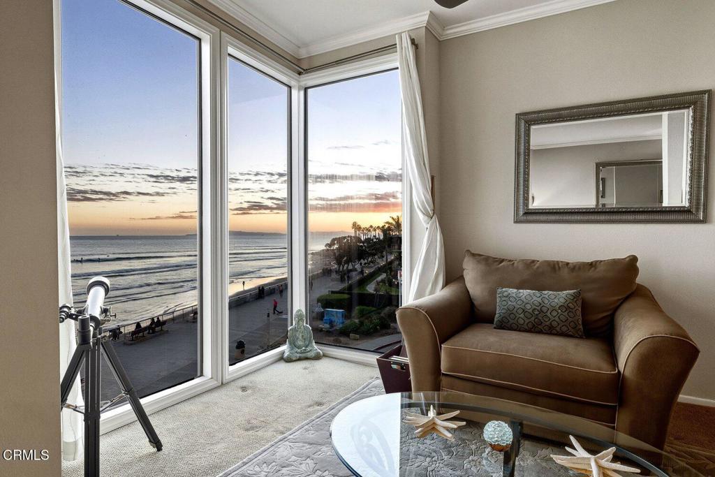 Living room with a brown armchair and telescope beside corner windows overlooking the ocean at sunset.