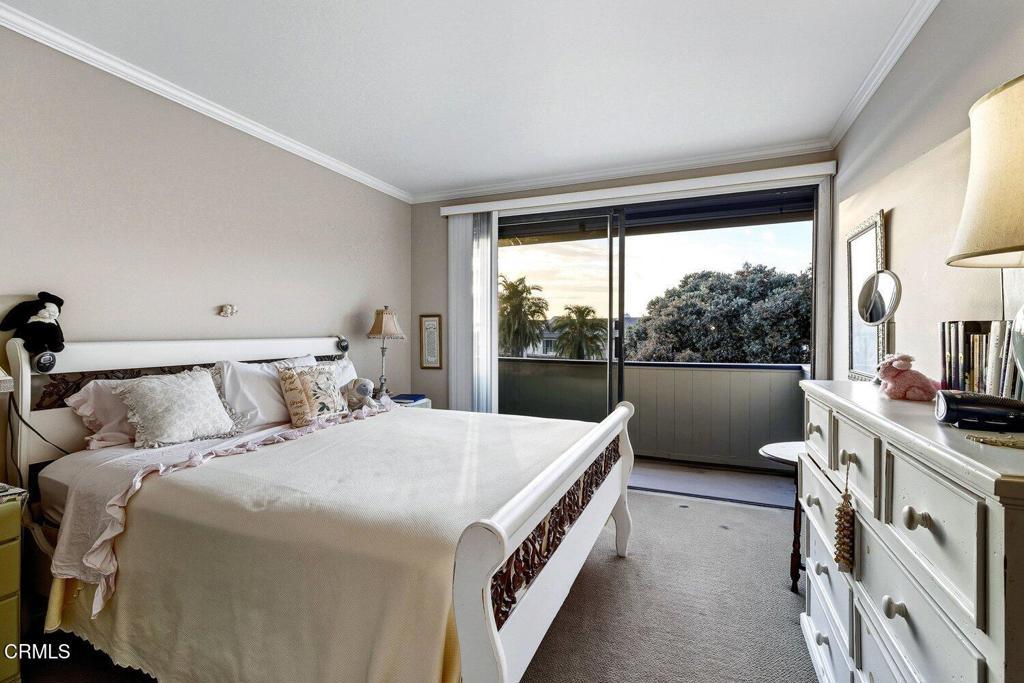 Furnished bedroom with a white bed and dresser beside sliding doors opening to a balcony.