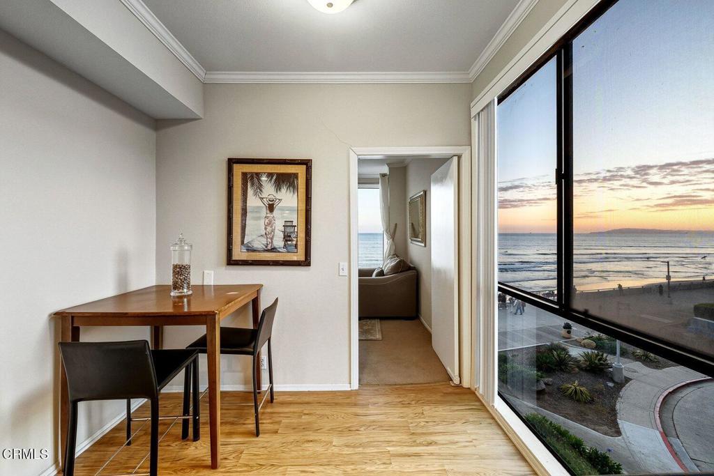 Dining nook with a wooden table and chairs overlooking the ocean through floor-to-ceiling windows at sunset.
