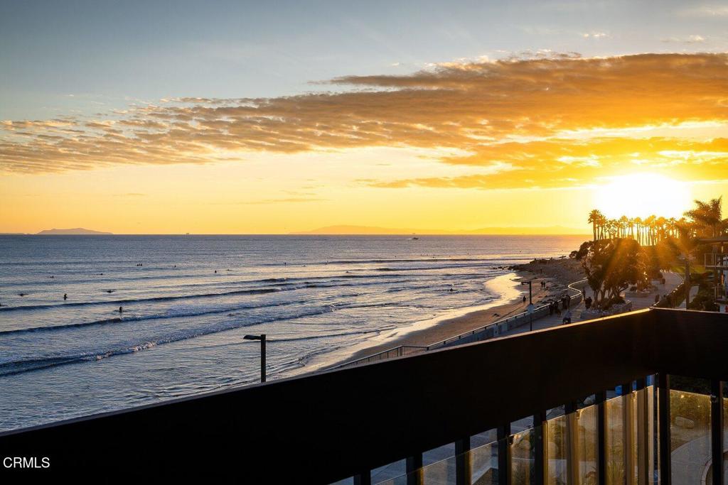 Ocean and beach at sunset, viewed over a glass balcony railing.