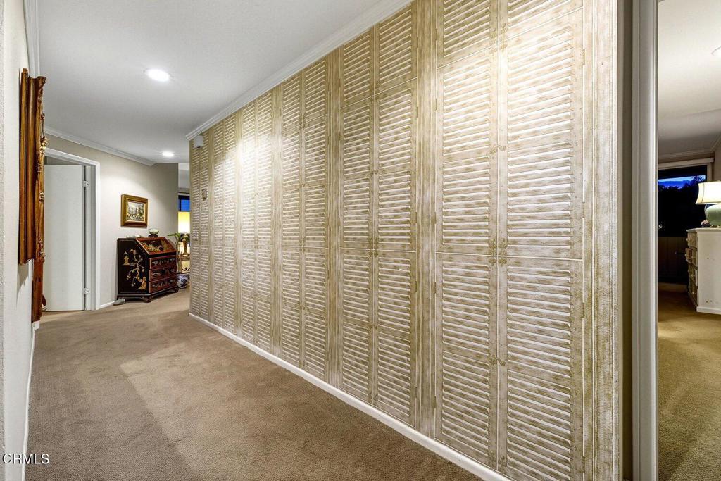 Carpeted hallway lined with tall louvered closet doors and a decorative chest at the far end.